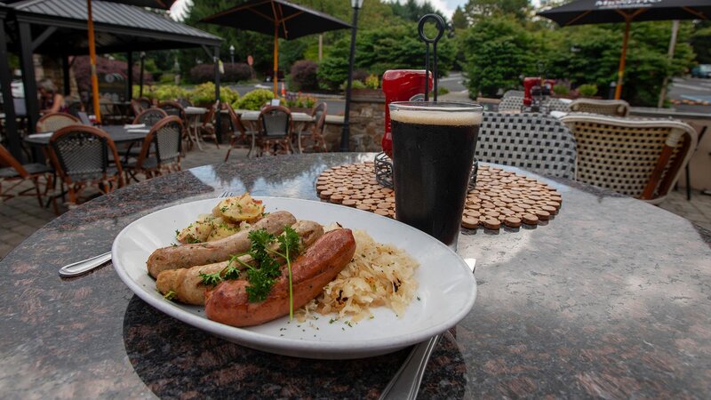Outside dining table with plated sausage entree with a pint of beer
